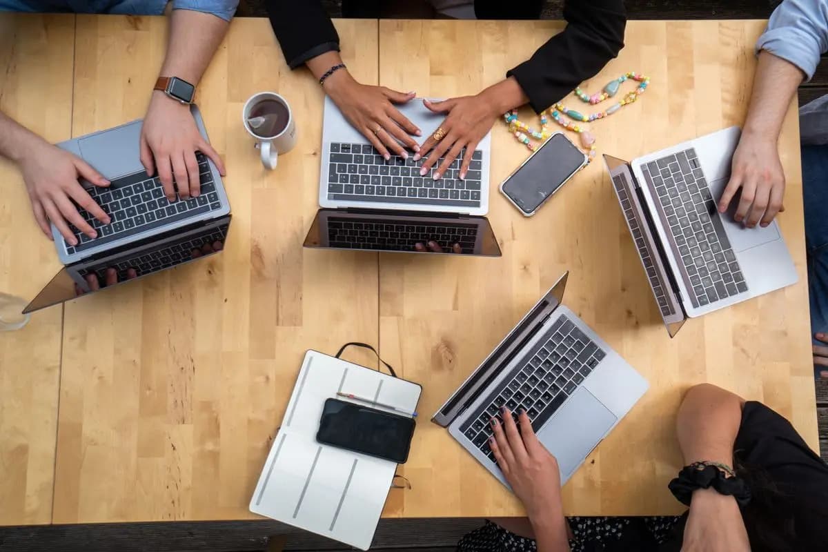 A group of individuals collaborating at a table, each focused on their laptops.